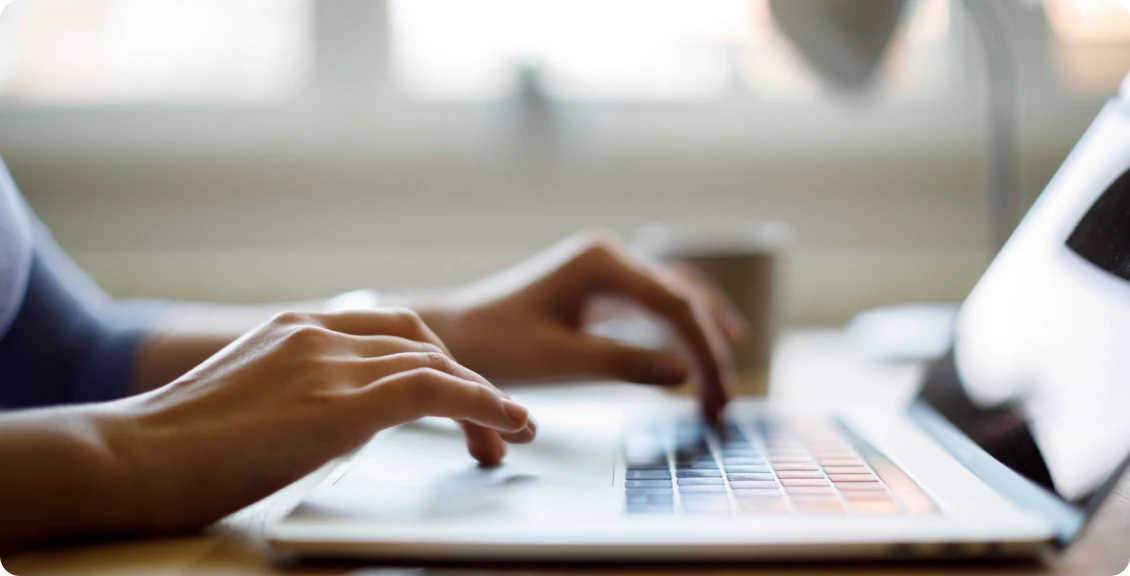 Hands typing on laptop keyboard by coffee mug