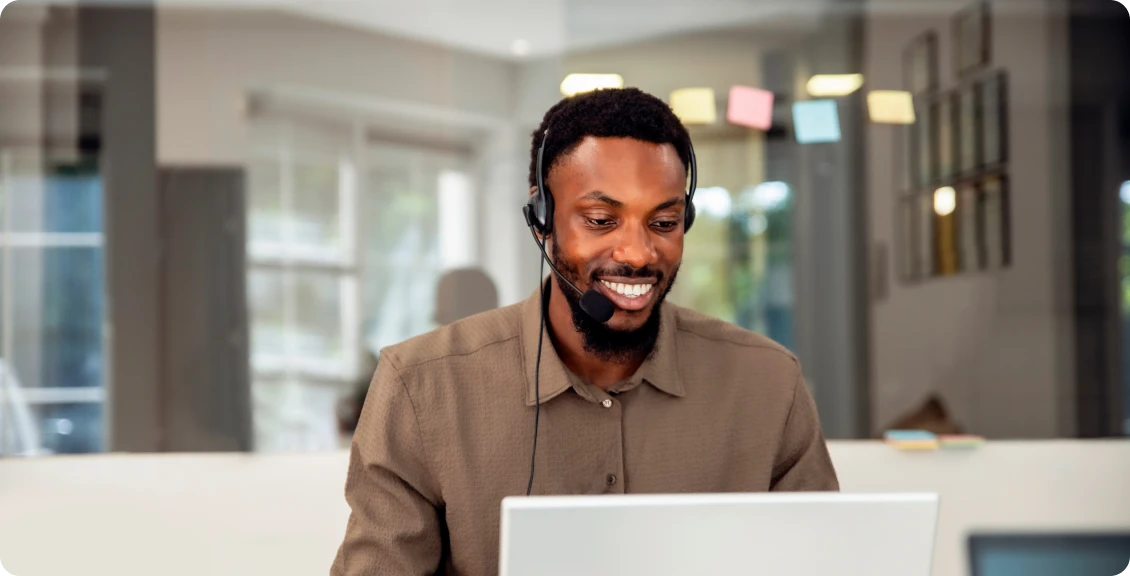 Smiling person with headset working on laptop